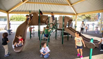 Children playing on a playground structure with climbers and slides with a large tin roof structure overhead.