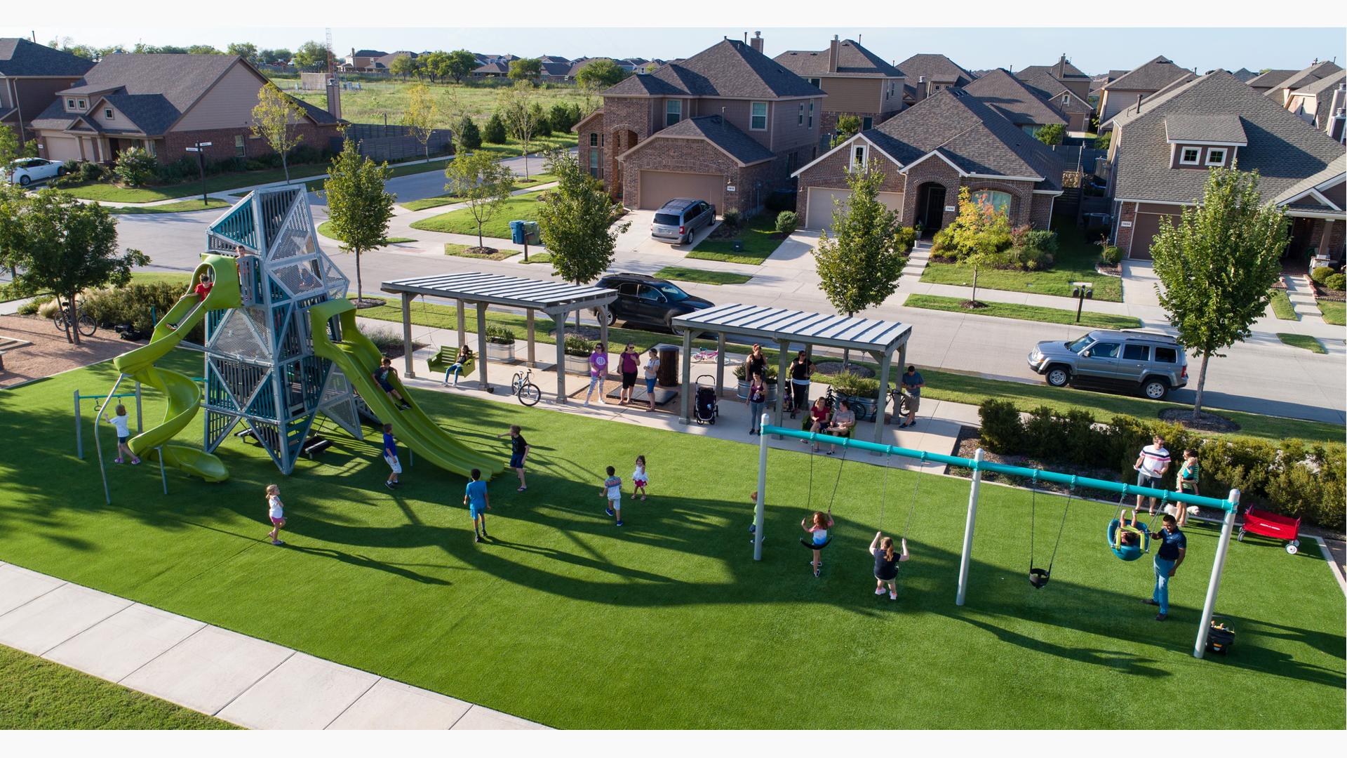 Parents watch their kids play on double swing set and custom Tower play structure in neighborhood Harvest Meadows park.