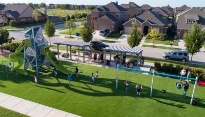 Parents watch their kids play on double swing set and custom Tower play structure in neighborhood Harvest Meadows park.