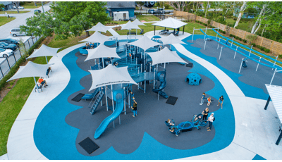 Families play on a inclusive playground colored with different shades of blue equipt with ramps, slides, climbers, and inclusive see-saws and gliders.