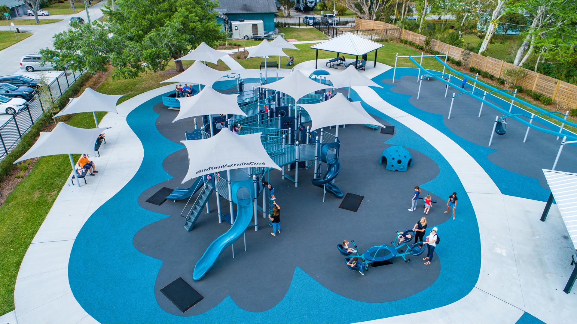 Families play on a inclusive playground colored with different shades of blue equipt with ramps, slides, climbers, and inclusive see-saws and gliders.
