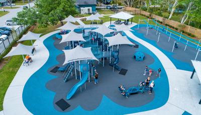 Families play on a inclusive playground colored with different shades of blue equipt with ramps, slides, climbers, and inclusive see-saws and gliders.