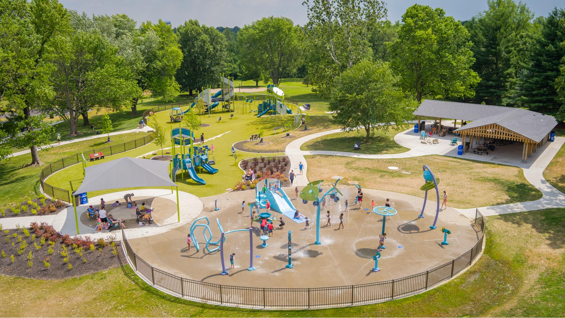 Elevated view of a city park with a splash pad and playground filled with playing children.