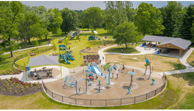 Elevated view of a city park with a splash pad and playground filled with playing children.