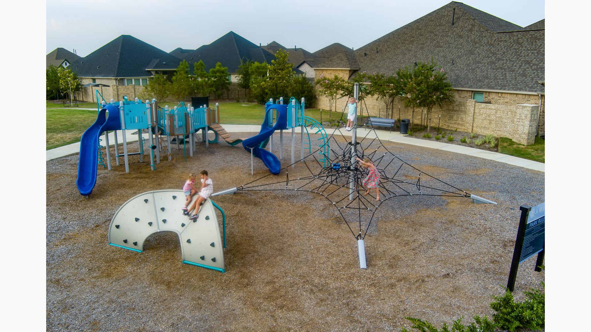Elevated view of children playing on a park playground with neighborhood housing in the background.