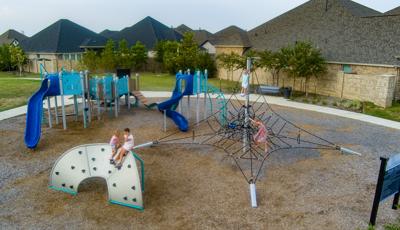 Elevated view of children playing on a park playground with neighborhood housing in the background.