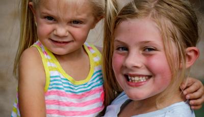 Girl in white shirt smiles as she holds little girl in striped shirt.