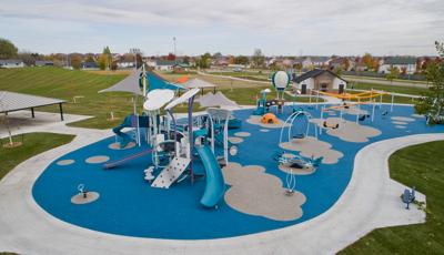 Large cloud and hot air balloon-themed play structures for all ages is surrounded by spinners, climbers, and swing set all set on a safety surfacing designed with grey cloud shapes. 