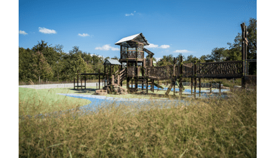 Nature-inspired playground with look-a-like log bridge. Playground is a two-story tower with a metal steel roof. 