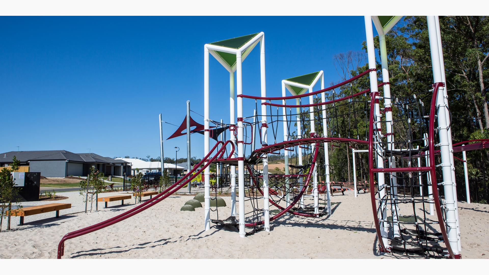 Custom GeoNetrix play structure sits on a sandy beach with trees behind it and a neighborhood across the street.