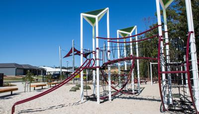 Custom GeoNetrix play structure sits on a sandy beach with trees behind it and a neighborhood across the street.