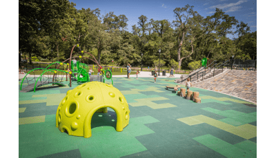 Families playing on the playground at a park with bright yellow green climbing structure and nature-like log steppers and balance beam.
