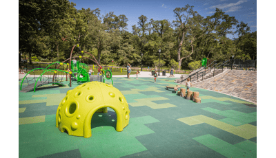 一家人在公园的操场上玩耍，公园里有明黄色的攀爬结构和自然般的原木台阶和平衡木。