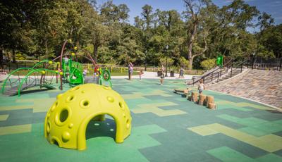 Families playing on the playground at a park with bright yellow green climbing structure and nature-like log steppers and balance beam.