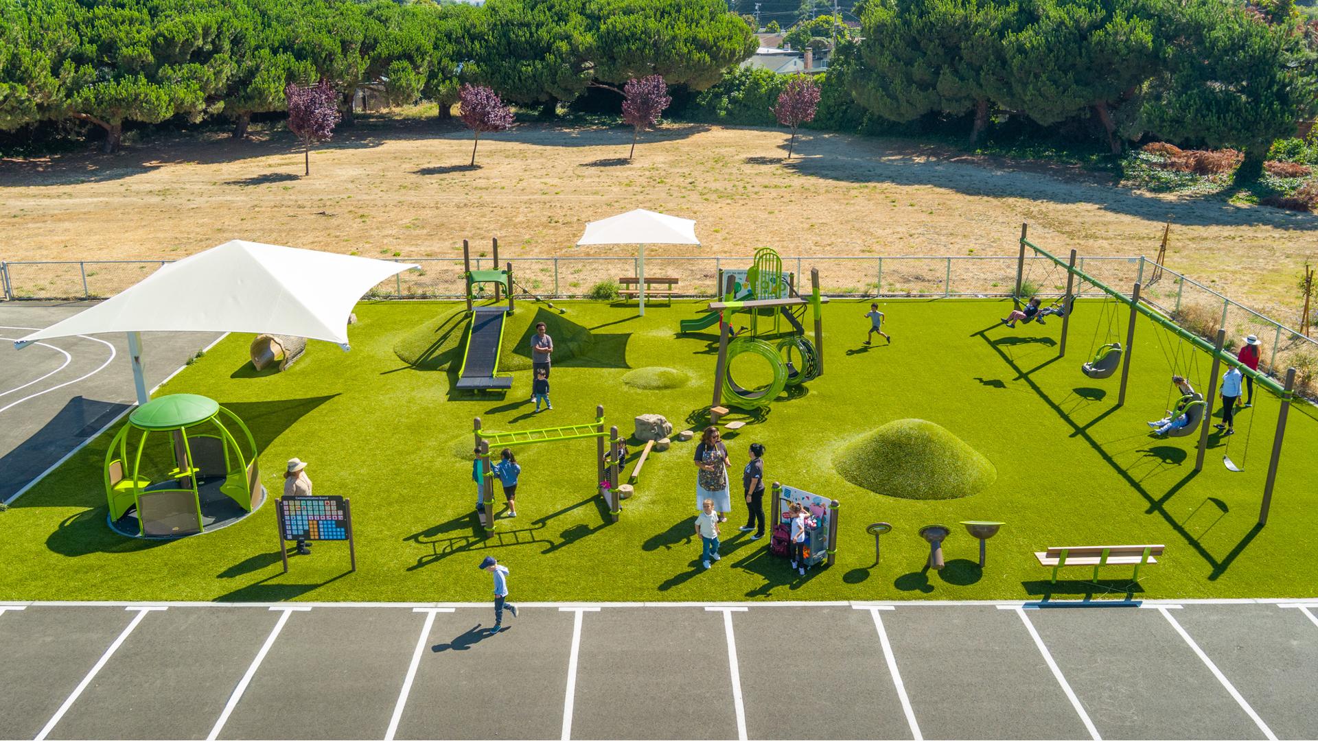 Elevated view of a artificially turfed rectangular play area with playground activities filled with children.