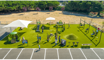 Elevated view of a artificially turfed rectangular play area with playground activities filled with children.