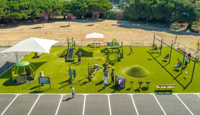 Elevated view of a artificially turfed rectangular play area with playground activities filled with children.