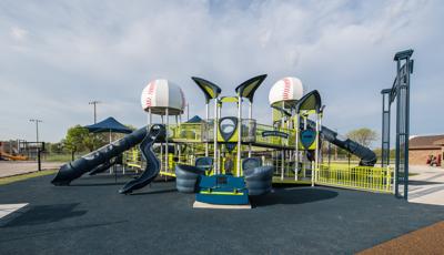 Green, blue and silver playground with 2 baseball dome roofs. Ramps and tall blue slides. Basketball courts in background.