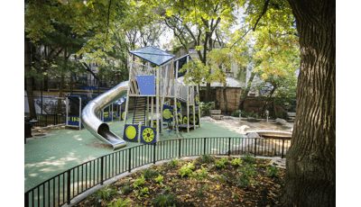 View past a large oak tree of a custom modern designed play structure with large stainless steel tubular slide. 