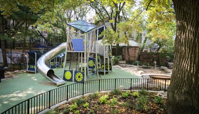 View past a large oak tree of a custom modern designed play structure with large stainless steel tubular slide. 