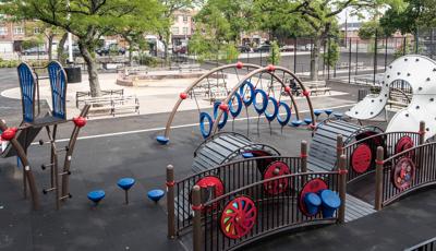 Mom helps her child down Evos slide in Paul Raimonda Playground, filled with climbers to play on.