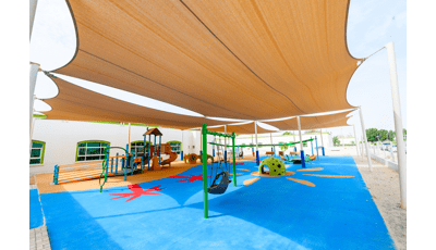 Large tan shade cover this play area with many inclusive playground elements including a ramped playground structure, single post swing, quiet area for kids to take a break and an accessible teeter totter all over colorful unitary surfacing.