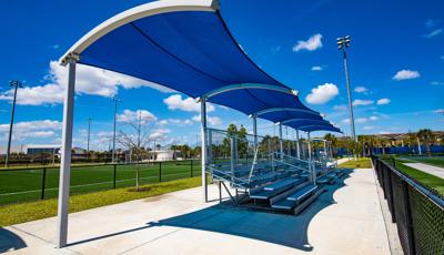 Blue curved shade located at an athletic field providing shade over bleachers. 