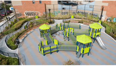 Full elevated view of an inclusive playground with accessible ramps and play panels set next to a brick building with a mural painted on the side.