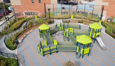 Full elevated view of an inclusive playground with accessible ramps and play panels set next to a brick building with a mural painted on the side.