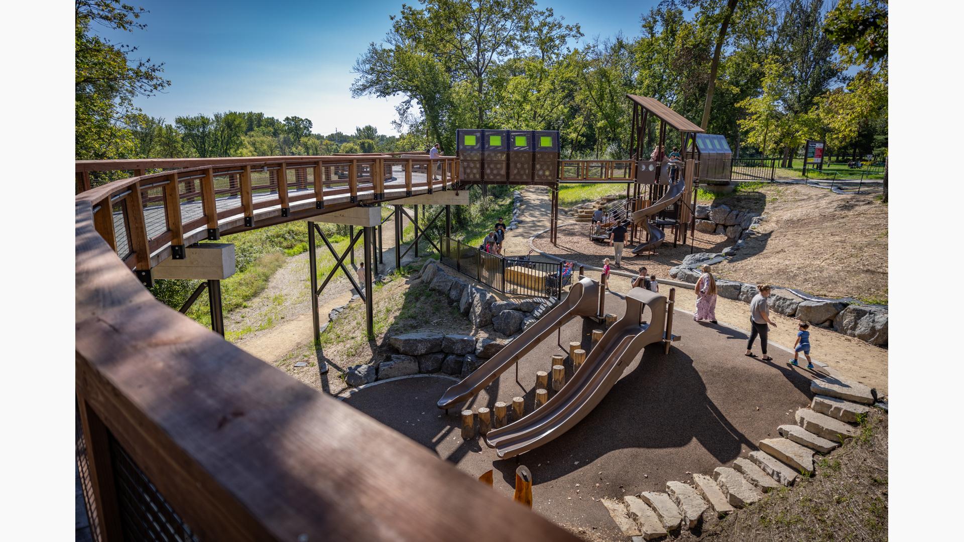 View down from a elevated walk way to a custom outdoor themed playground and play area.