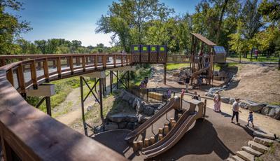 View down from a elevated walk way to a custom outdoor themed playground and play area.