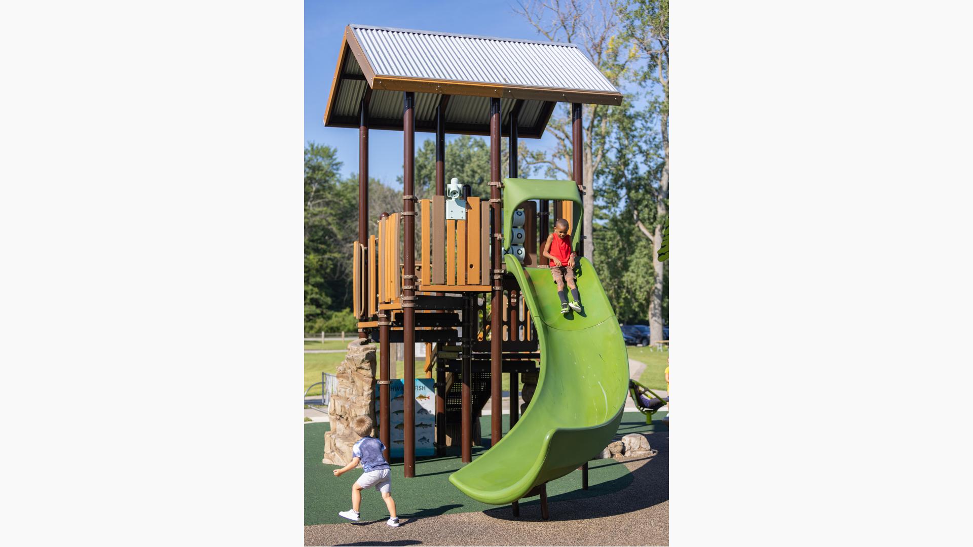 A natural wood-looking play structure with apple green Alpine Slide by Landscape Structures.