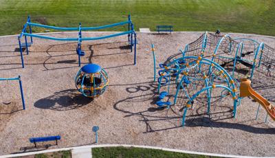 Elevated view of a park playground with blue posts as children climb through the weaving ropes and belt climbers of the play structure.