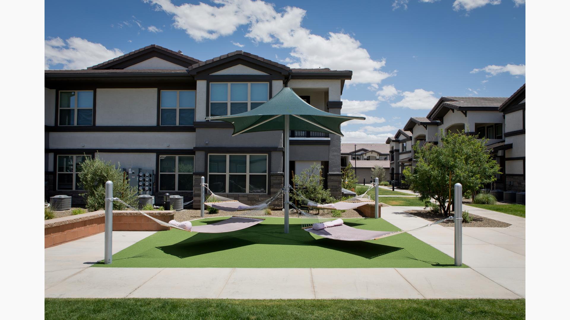 Four hammocks tied to a center post with green shade in residential courtyard. 