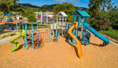 Two colorful tower structures connected by bridges and climbers great a large playground all on a wood chip surfacing. 