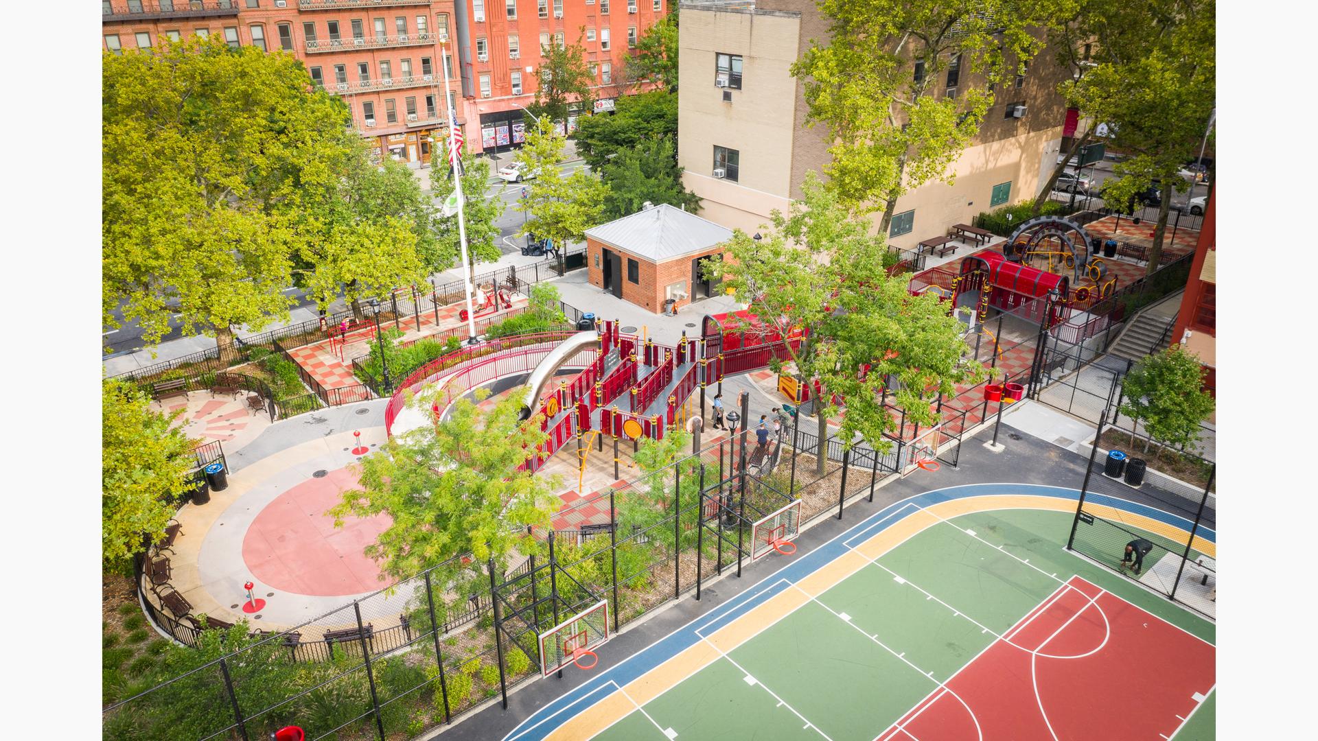 Aerial view of a playground park amongst city buildings surrounded by black wire fencing next to multiple basketball courts.