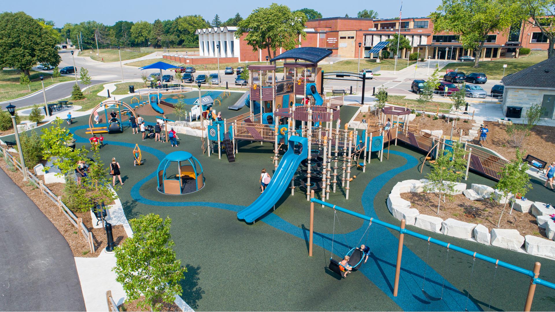 Elevated view of a large play area with a inclusive accessible play structure surrounded by multiple wheelchair accessible spinners and swings. 