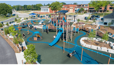 Elevated view of a large play area with a inclusive accessible play structure surrounded by multiple wheelchair accessible spinners and swings. 