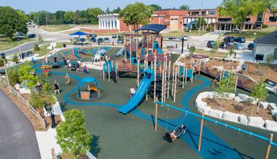 Elevated view of a large play area with a inclusive accessible play structure surrounded by multiple wheelchair accessible spinners and swings. 