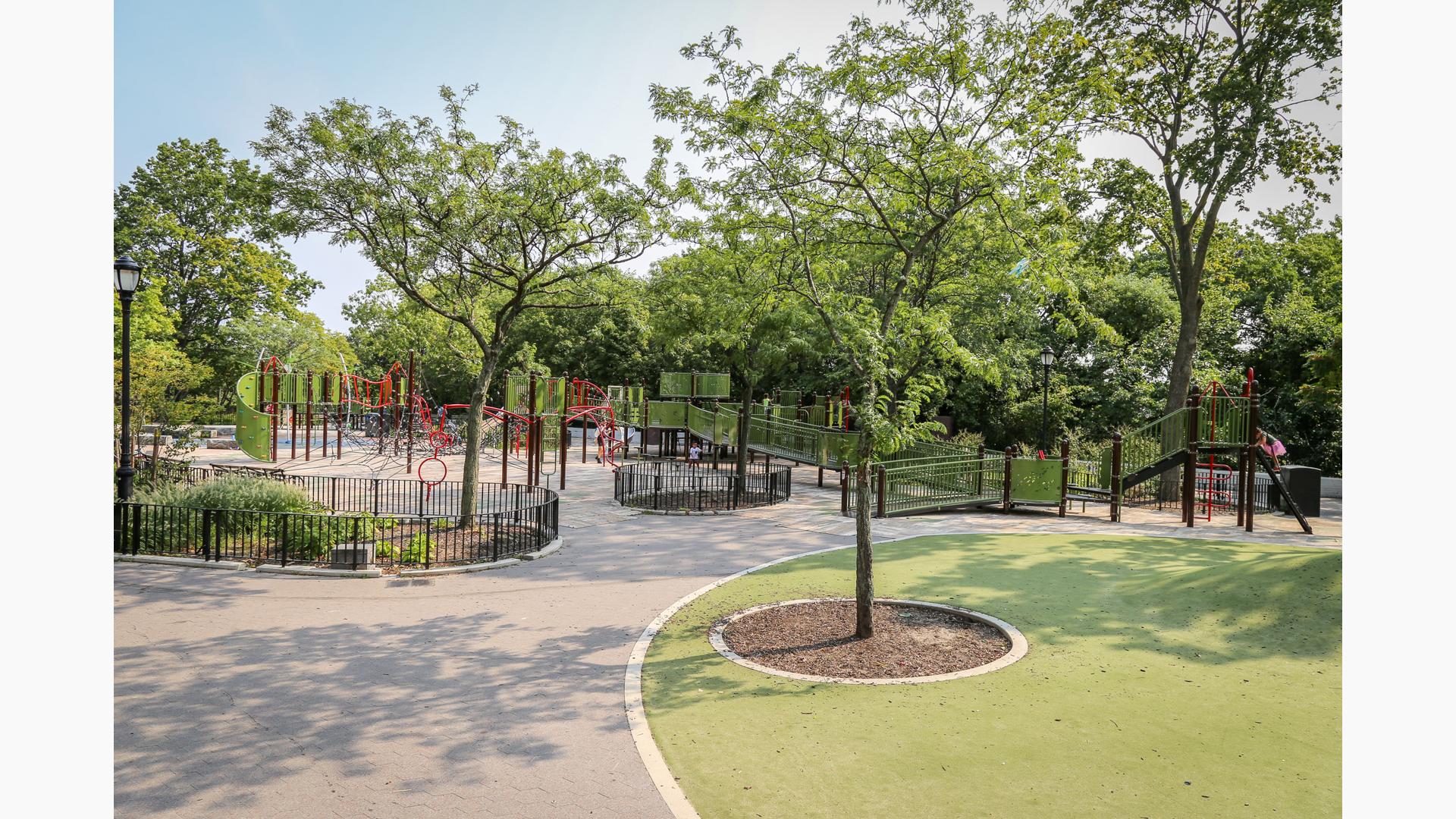 Surrounding trees are contained behind black fencing as a large inclusive playground winds around the near by gardens and trees of the park.