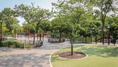 Surrounding trees are contained behind black fencing as a large inclusive playground winds around the near by gardens and trees of the park.