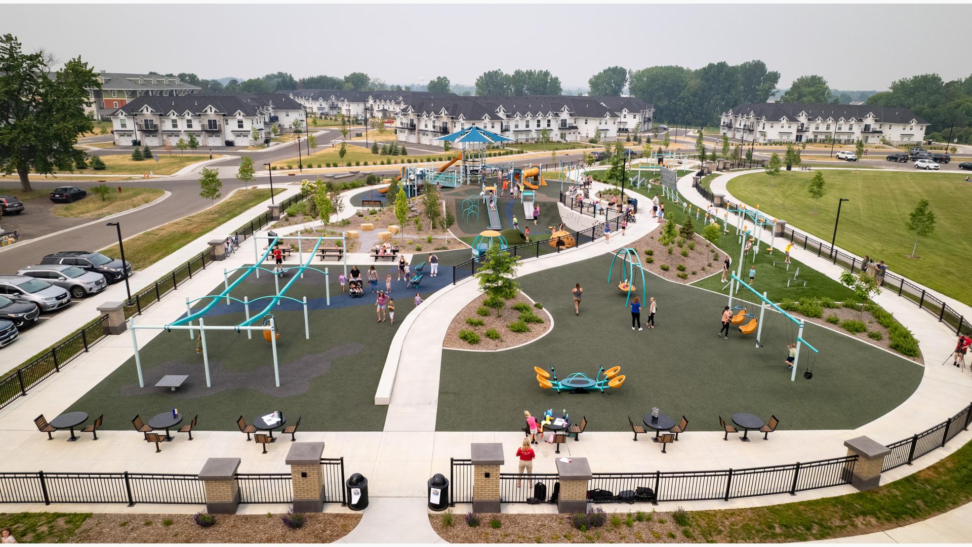 Elevated view of a large inclusive playground incorporated into the small hilled landscape of the park with a town home development in the background.