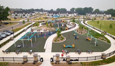 Elevated view of a large inclusive playground incorporated into the small hilled landscape of the park with a town home development in the background.