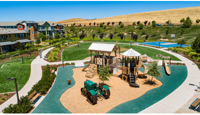 Farm-themed playground structure with green tractor, barn and haybale stairs in residential park. 