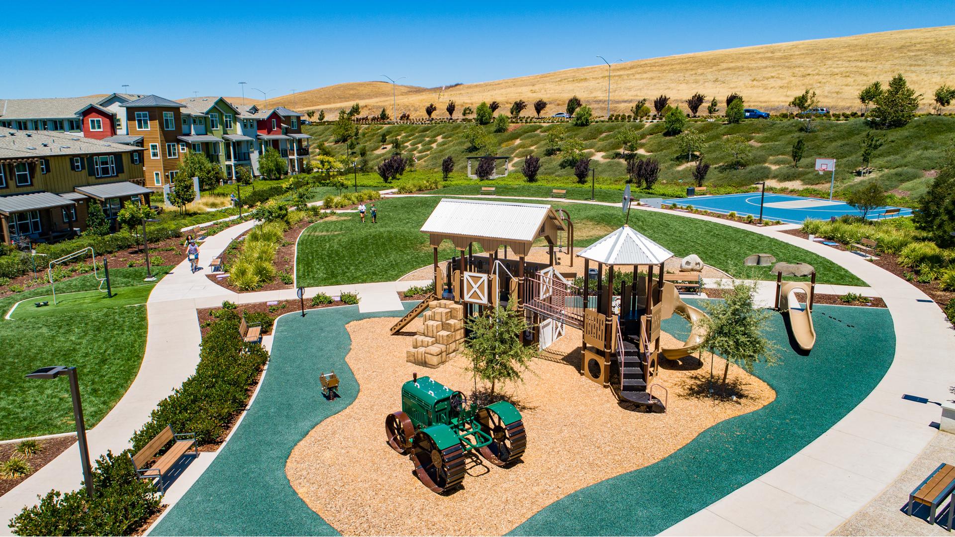 Farm-themed playground structure with green tractor, barn and haybale stairs in residential park. 