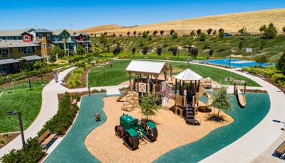 Farm-themed playground structure with green tractor, barn and haybale stairs in residential park. 