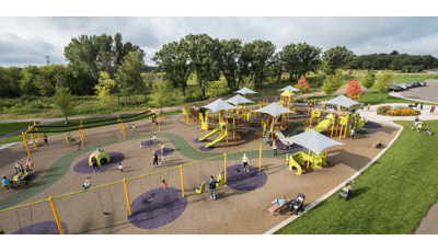 Aerial view of large playground with kids and families playing on swings, ziplines and playground. Playground is colors include bright green slides and climbers with gray shade. 