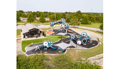 Three geometric blue and silver playground areas for all ages in park location. The playground tower includes three pods with an enclosed connected walkway.  The surfacing is design with stars and planets to round out the space theme play space. 