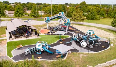 Three geometric blue and silver playground areas for all ages in park location. The playground tower includes three pods with an enclosed connected walkway.  The surfacing is design with stars and planets to round out the space theme play space. 