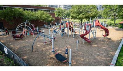 Children play on the many activities of a park playground next to a brick building. 
